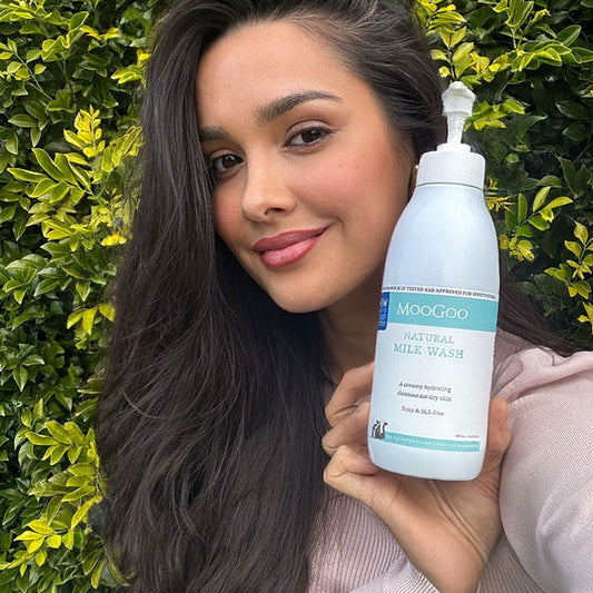 Woman smiling while holding MooGoo Natural Milk Wash, gentle hydrating cleanser for sensitive face and body