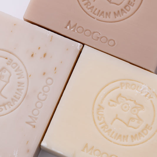 Three MooGoo soap bars photographed closely to show branding stamp and natural finish, including smooth buttermilk and speckled oatmeal varieties