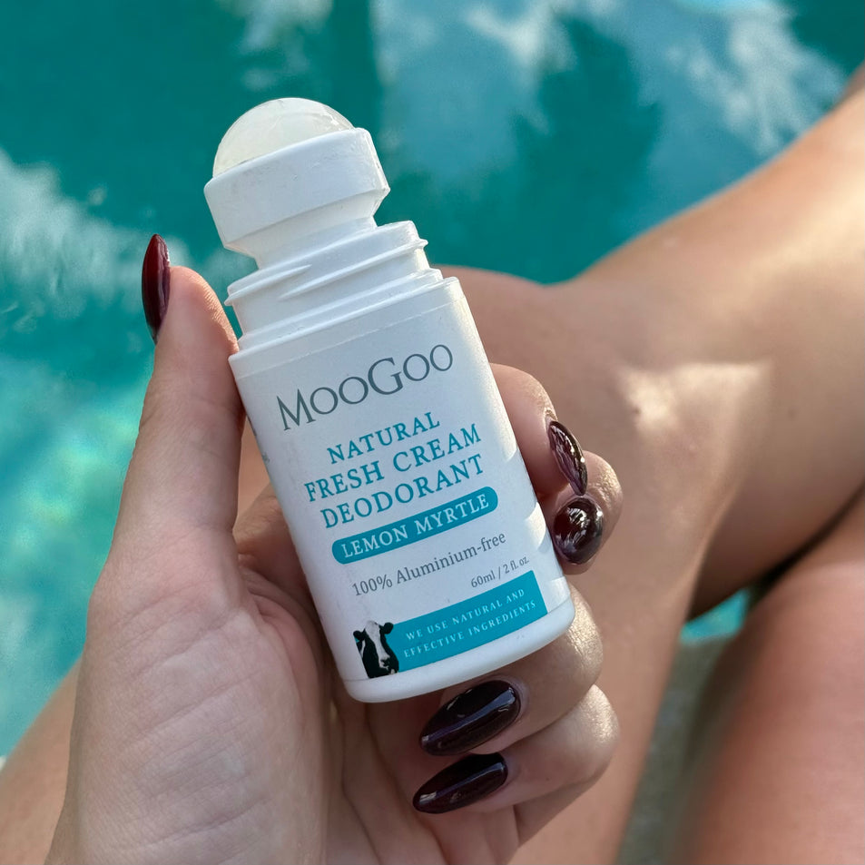 MooGoo Natural Lemon Myrtle Fresh Cream Deodorant 60ml held by a hand with a pool background.