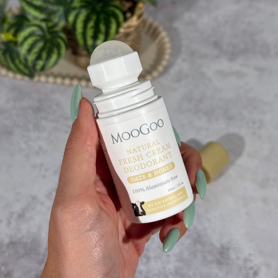 MooGoo Natural Oats & Honey Fresh Cream Deodorant 60ml held by a hand with a tiled background and a plant on a tray.