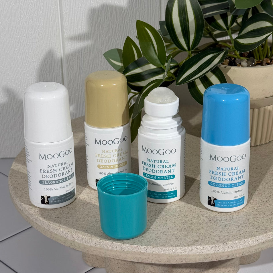All four MooGoo Natural Fresh Cream Deodorants 60ml on a tray with a plant in the background. Includes Sensitive & Fragrance Free with a white lid, Oats & Honey with a caramel lid, Lemon Myrtle with a green/teal lid and Coconut Cream with a blue lid.