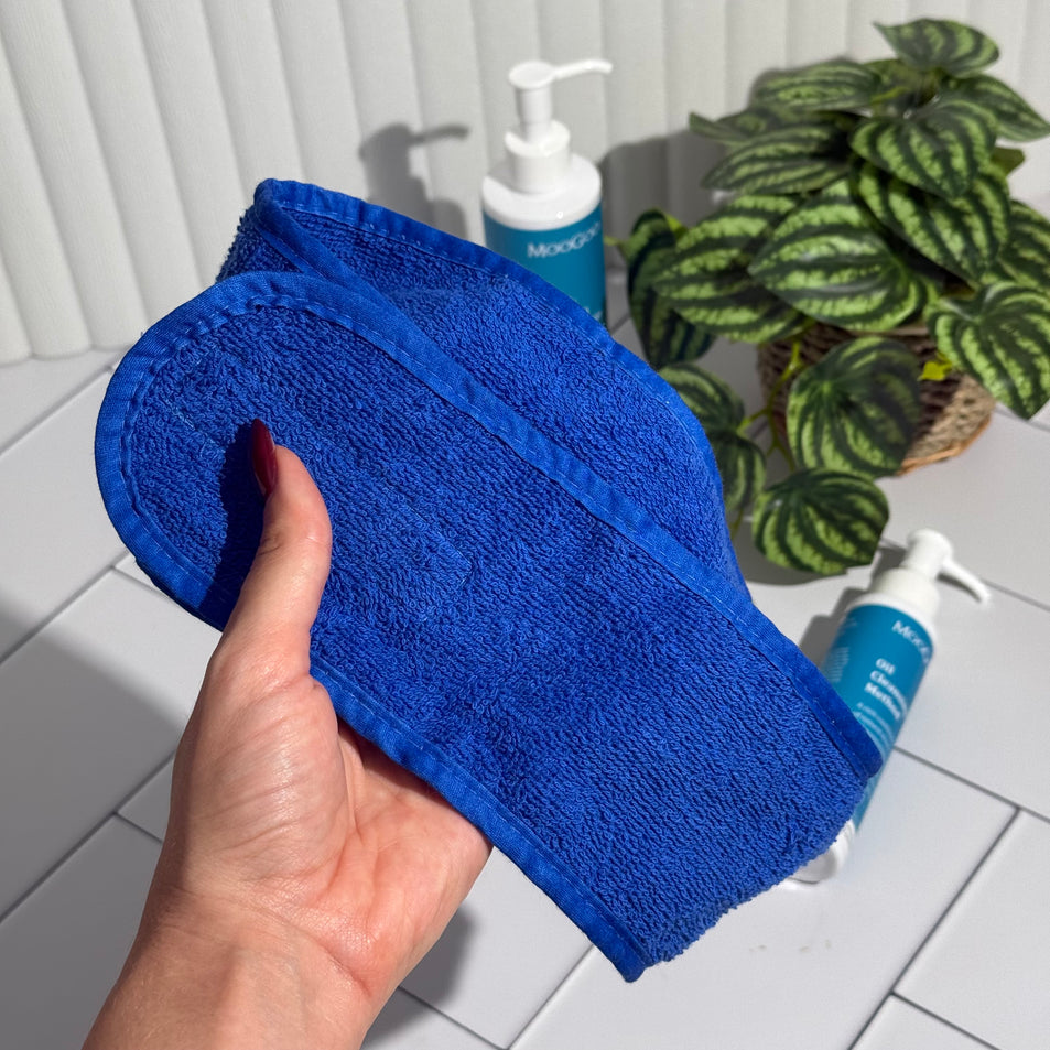 Blue terry toweling Headband with a MooGoo label, held by a hand with MooGoo Face Cleansers and a plant in the background.