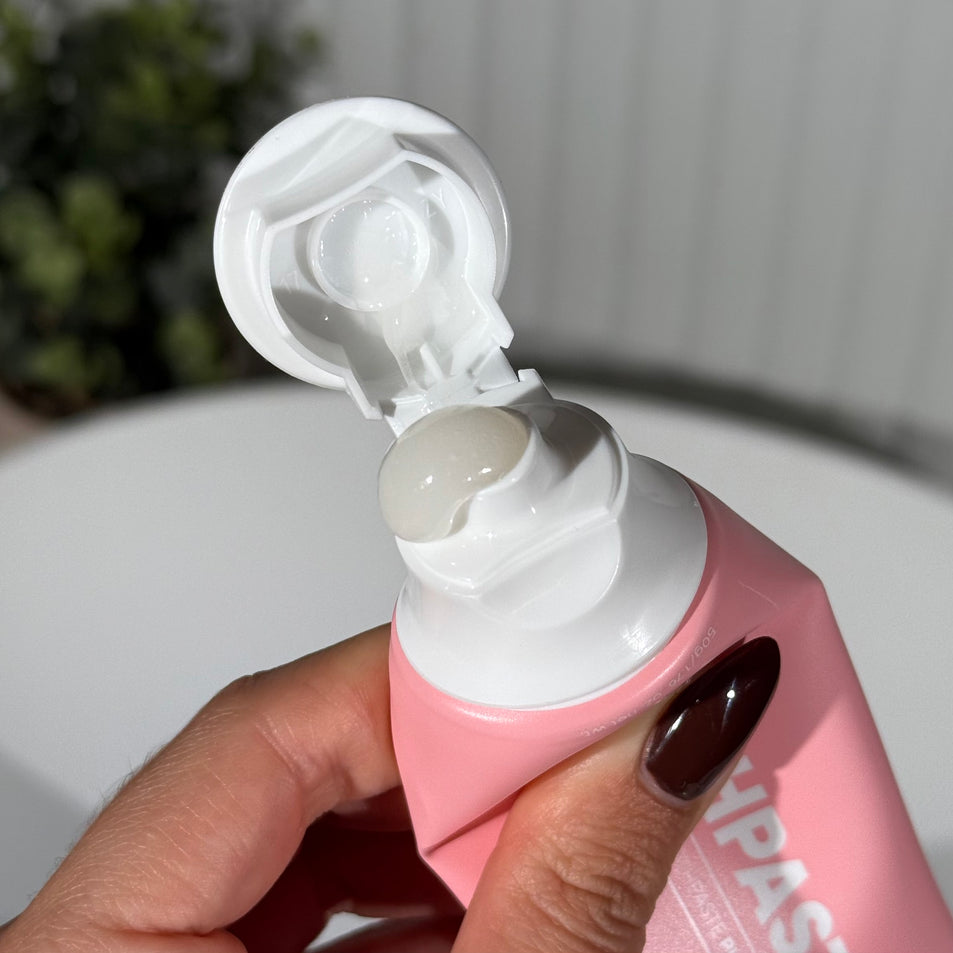 Hand holding a tube of MooGoo Mini Moo Strawberries and Cream kids toothpaste and squeezing out the toothpaste. Healthy habit building, tastes like strawberries. Fluoride-free formula, safe for kids. Safe if swallowed. 