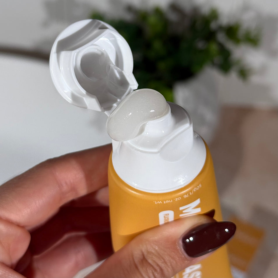 Hand holding a tube of MooGoo Mini Moo Vanilla Ice Cream kids toothpaste and squeezing out the clear toothpaste. Healthy habit building, tastes like vanilla. Fluoride-free formula, safe for kids. Safe if swallowed. 