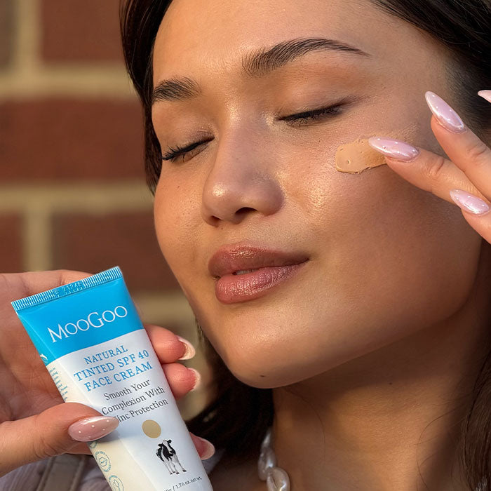 Woman applying MooGoo Natural Tinted SPF 40 Face Cream to her face - smooth complexion, reduce redness, hydrate skin. Perfect under makeup, for all skin tones and Eczema safe SPF.