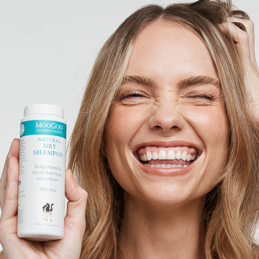 MooGoo Dry Shampoo lifestyle photo, smiling woman holding bottle of talc free scalp friendly formula for adding volume and reviving hair.
